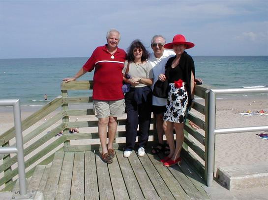 Friends pose together on a wooden deck overlooking the beach and ocean, enjoying a sunny afternoon.