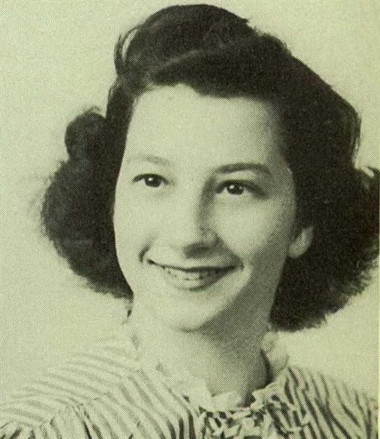 A cheerful young woman poses with a bright smile, embracing a classic hairstyle typical of her era.