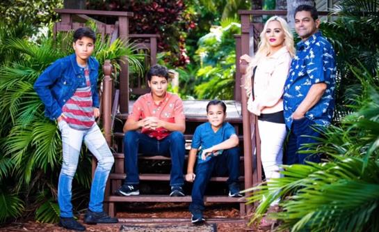 A family poses on wooden steps with tropical plants, showcasing their playful spirit and style.