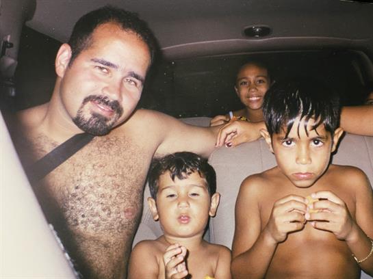 A man sits in a car with two boys, sharing a joyful moment while another child smiles behind them.