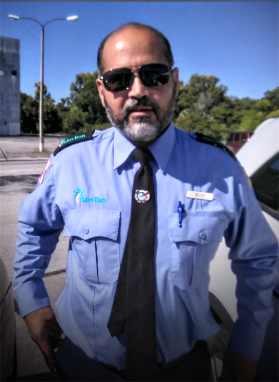 A security officer in a blue uniform with sunglasses poses near parked cars on a sunny day.