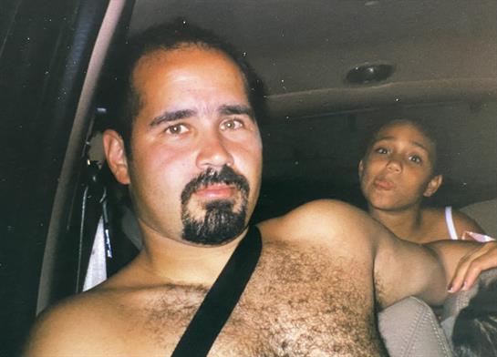 A confident man drives in front while a child watches from the back during an evening ride.