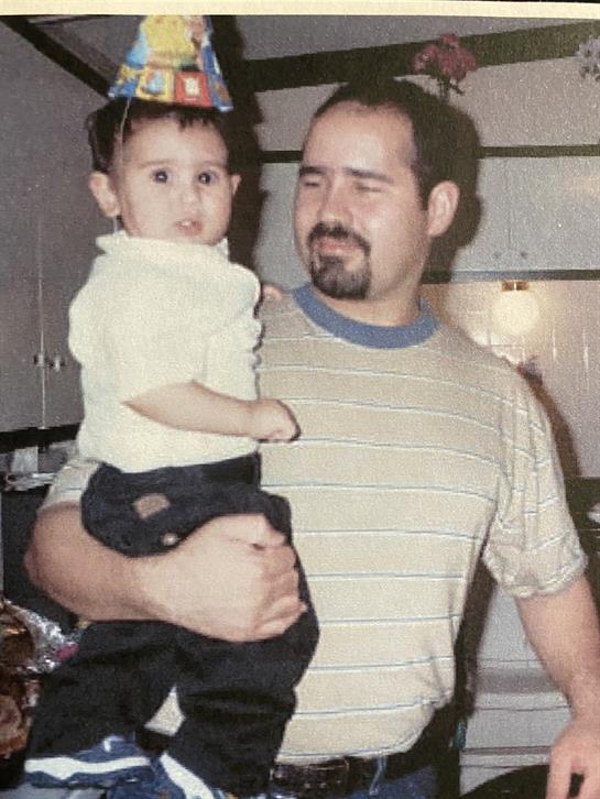 A father smiles while carrying his child, creating a joyful moment in a cozy kitchen.