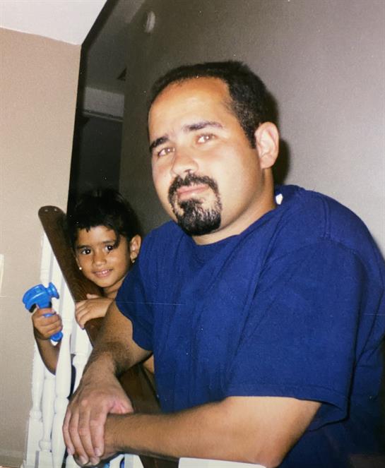 A man relaxes on the staircase while a young boy playfully hides behind him with a toy.