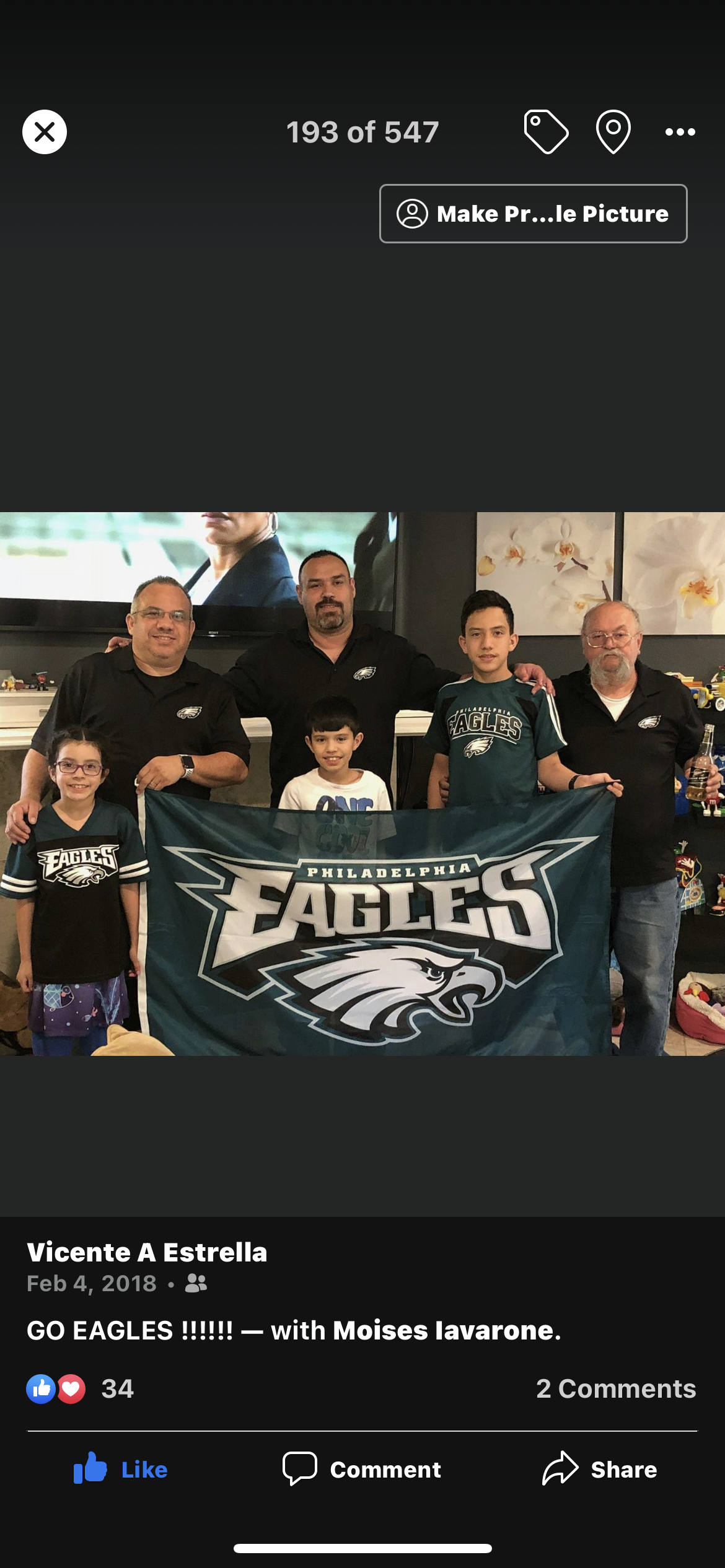 Group of men and children proudly display Eagles banner while celebrating together.