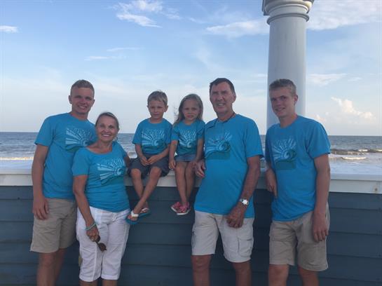 Six family members pose happily on a seaside wall, enjoying their time together outdoors.