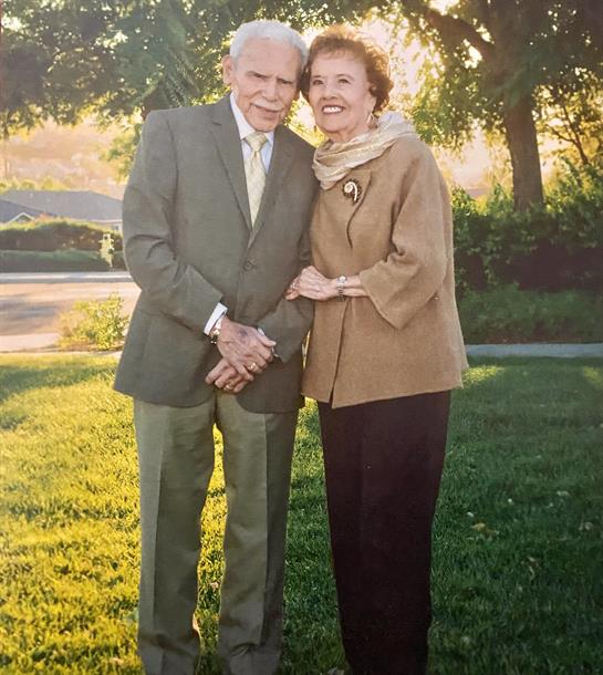 Elderly couple stands close in a park, smiling warmly during a sunny afternoon.