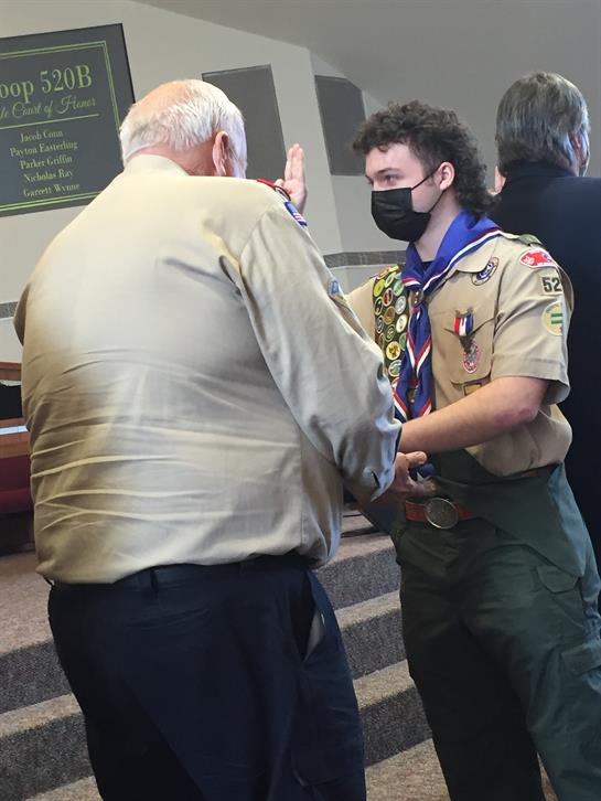 A young scout is being honored by a leader during an award ceremony at a community center.
