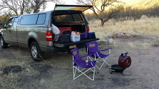 A parked truck with an open tailgate displays camping gear in the desert.