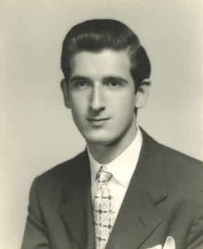 A young man dressed in a suit and tie poses confidently in a studio, showcasing classic style.