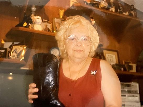 Senior woman holds a black vintage boot while smiling in a warmly decorated room.