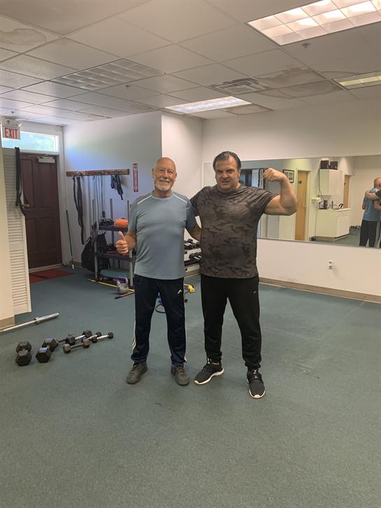 Men smile while showcasing weightlifting progress in a well-equipped gym.