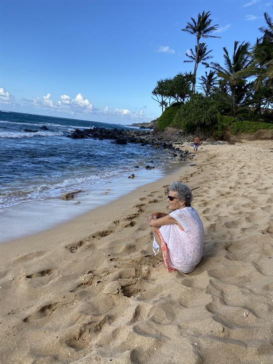 A woman sits quietly on a sandy beach, enjoying the calming sound of ocean waves on a sunny day.