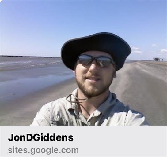 Man enjoys a sunny day by the shore while walking along the water's edge, smiling at the camera.