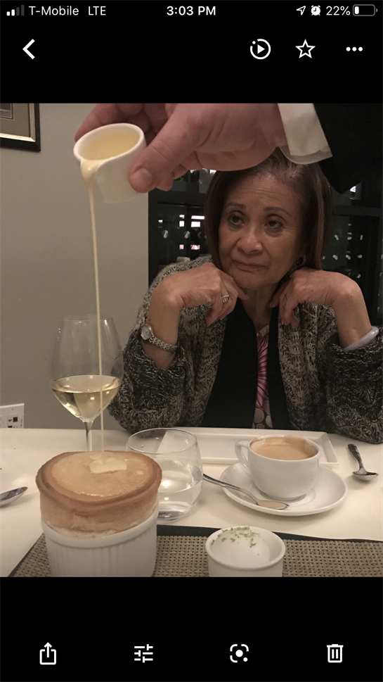 A woman gazes at a dessert while someone pours sauce in an intimate dining experience.