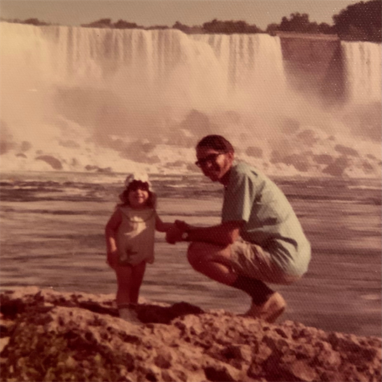 A child and her grandparent play near the Iguazu Falls, enjoying a warm sunny day together.