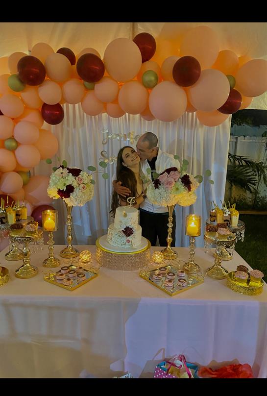 A couple shares a romantic kiss in front of a beautifully decorated table featuring a wedding cake.