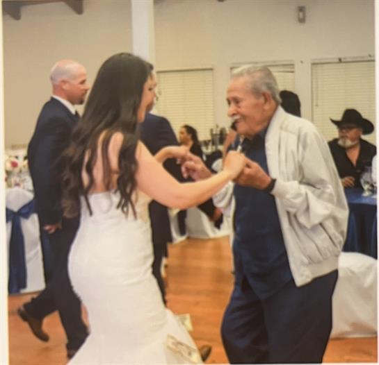 A young woman dances happily with an older man at a lively event, surrounded by guests.