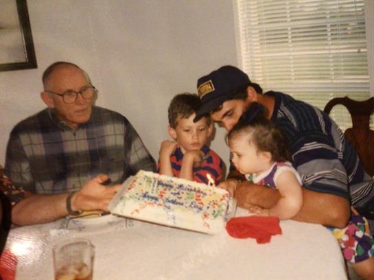 Family members gather to celebrate a birthday, observing children curiously looking at a cake.