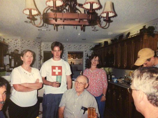 Family members enjoy drinks and conversation in a warm kitchen setting filled with smiles.