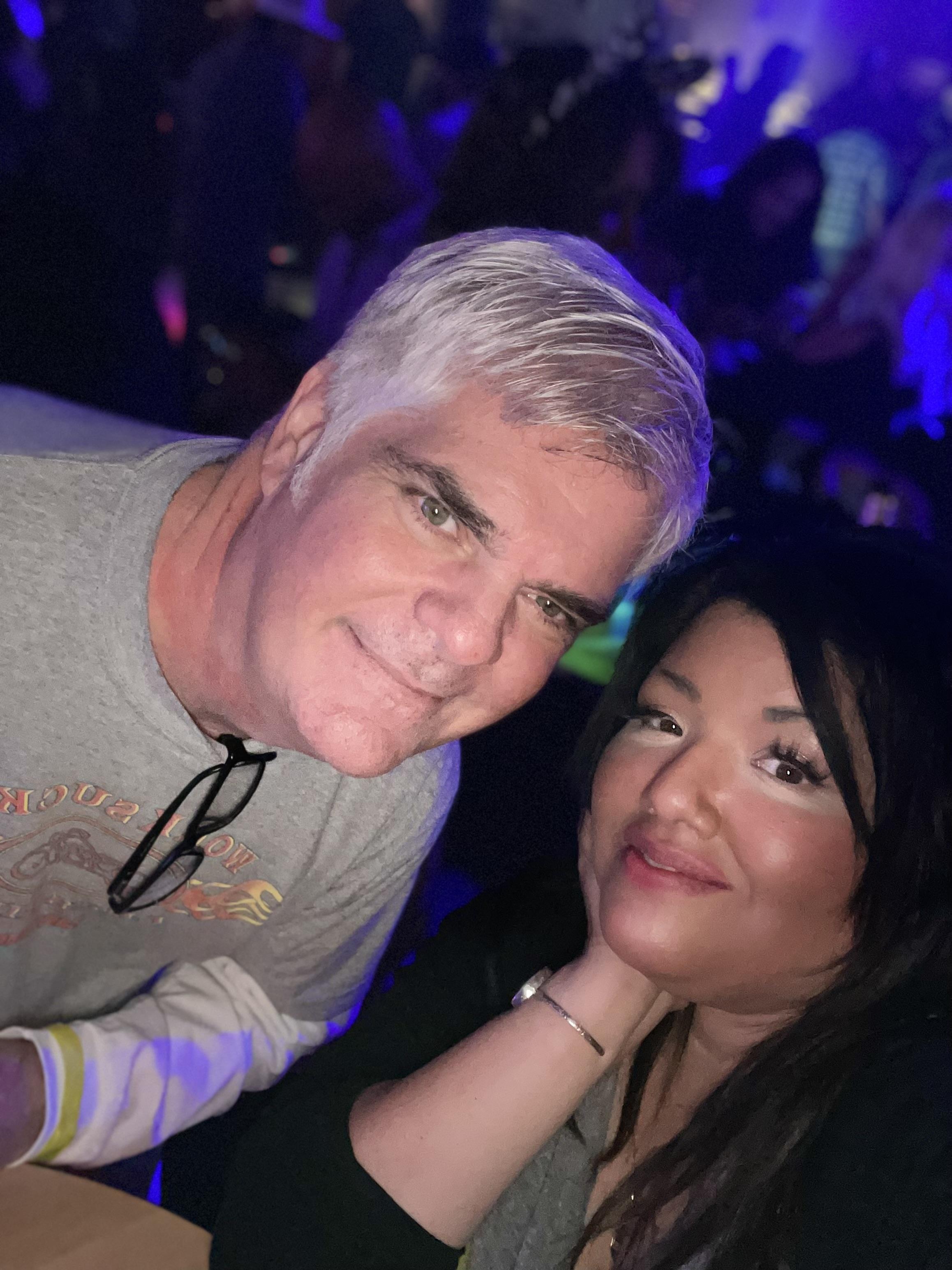 Two people smiling together at a lively music event in a colorful atmosphere.