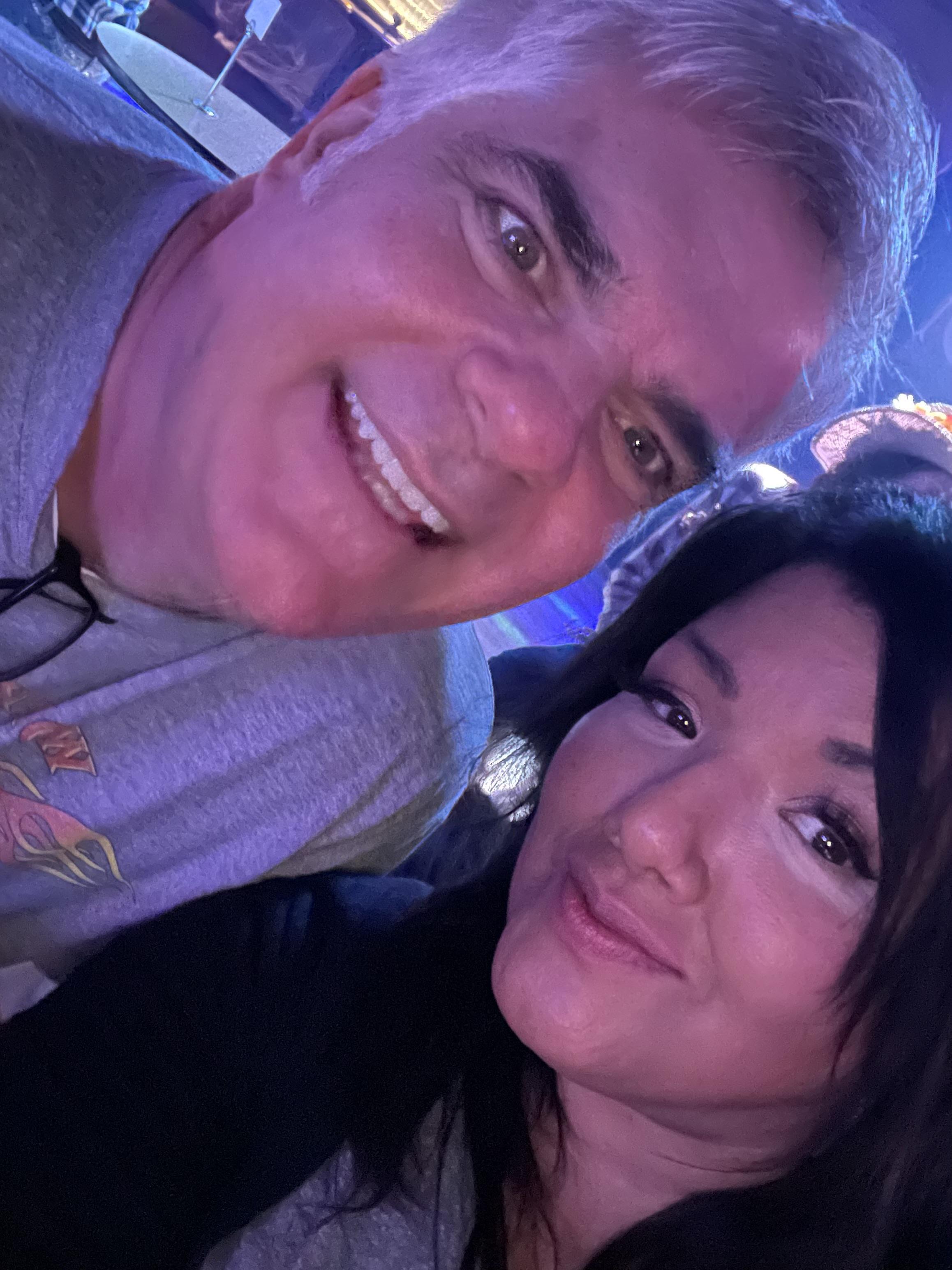 Two friends take a cheerful selfie while enjoying a lively concert at night.