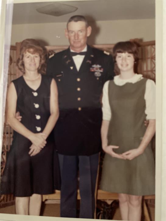 A soldier stands proudly with two women, celebrating a special occasion in a cozy setting.