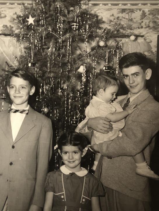 Siblings and cousins share a joyful moment beside a beautifully decorated Christmas tree.