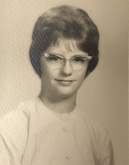 Portrait of a young woman in the 1960s, wearing glasses and a simple blouse, smiling gently.