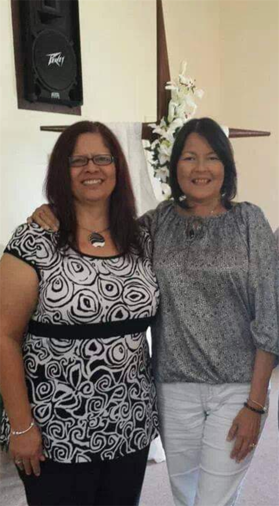 Two women pose happily with arms around each other at a joyful family event.