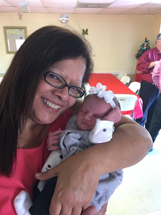 A grandmother smiles brightly while holding her newborn grandchild in a festive atmosphere.
