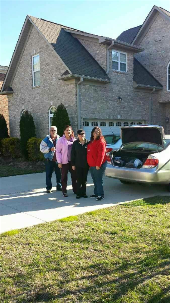 Four family members stand in a driveway, smiling as they prepare to leave on a trip.