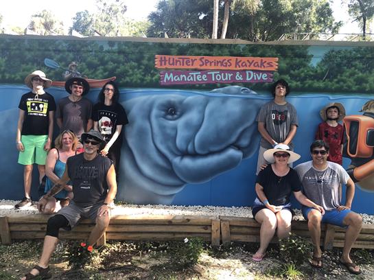 Friends enjoy a group photo in front of a vibrant mural after a fun kayaking tour.