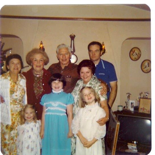 A nostalgic family reunion with eight members posing happily in a warmly decorated room.
