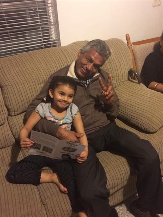 Grandfather and granddaughter enjoy quality time on a couch, sharing smiles and laughter together.