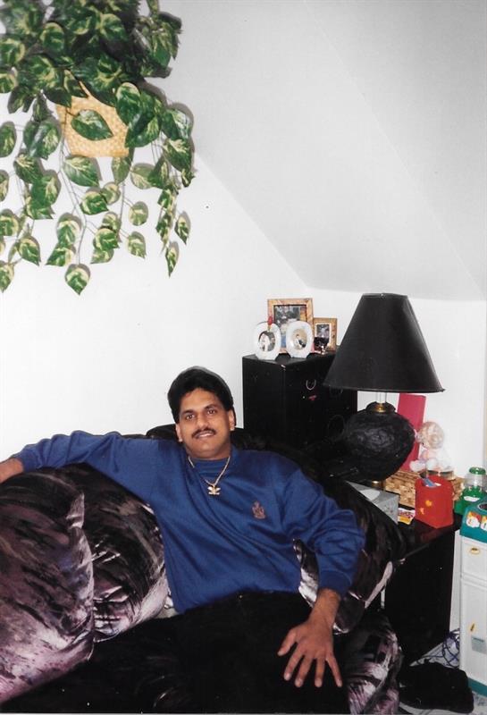 A man lounges comfortably on a dark couch in a welcoming living room filled with plants.