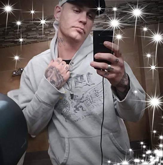 A young man in a gray hoodie and cap takes a tattooed selfie in the bathroom.