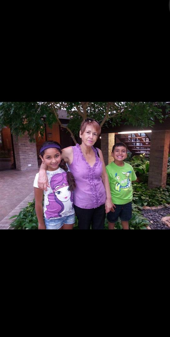 A woman stands with two children in a lush garden, all sharing joyful smiles in a warm moment.