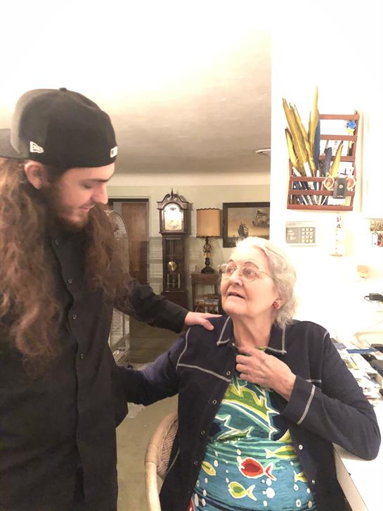 A young man and an elderly woman share a heartfelt chat at home, amidst family artifacts.