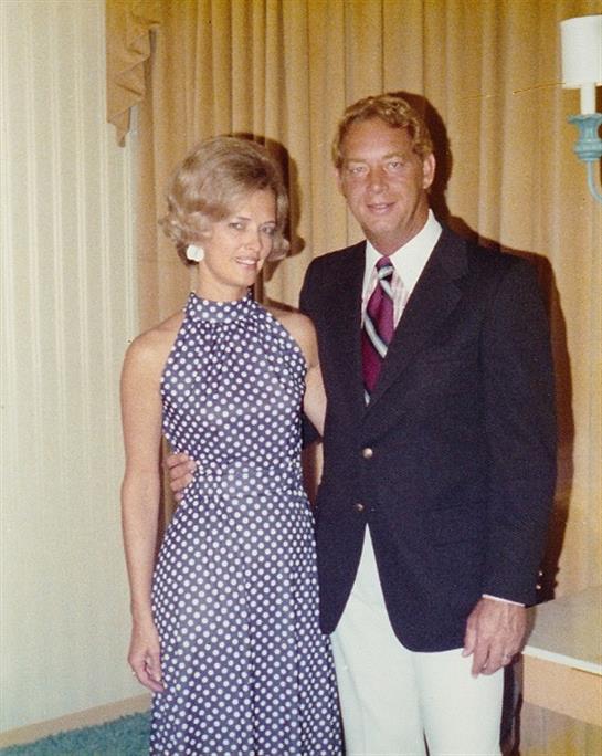A couple poses for a picture, dressed in stylish vintage clothing, at a formal gathering.
