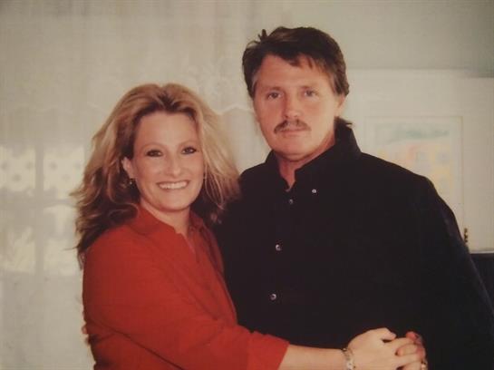 A couple stands close, sharing a warm smile while enjoying each other's company indoors.
