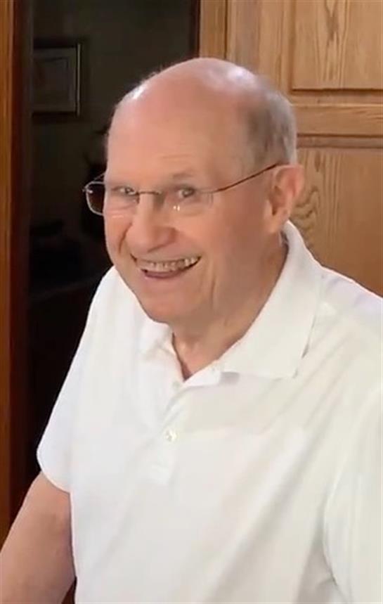 An elderly man with glasses enjoys a cheerful moment at a table in a bright home.