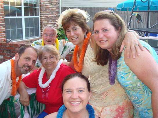 Family members enjoy a joyful luau party in a backyard, wearing colorful leis and smiling.