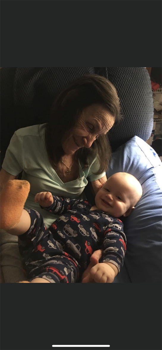 Grandmother shares a loving interaction with her smiling baby grandson while sitting on a couch.