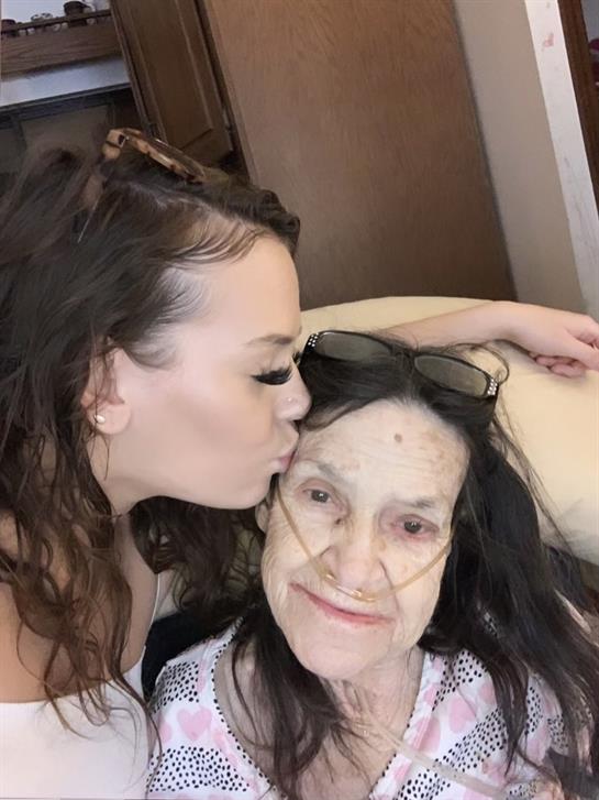 A granddaughter kisses her grandmother lovingly while sitting together in a warm, inviting room.