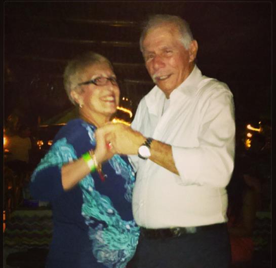 Elderly couple shares a joyful moment dancing together at a vibrant evening celebration.