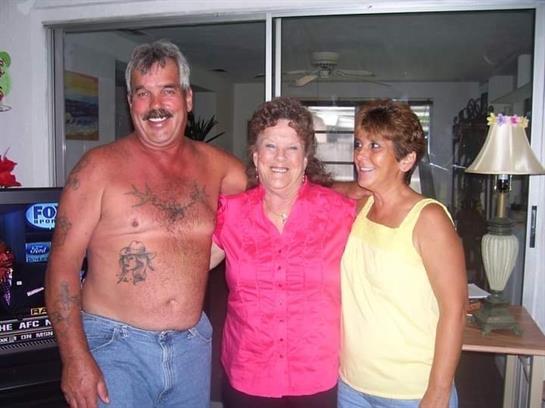 Three family members smile together inside a bright room adorned with plants and cheerful decor.