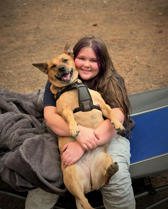 A smiling girl holds her happy dog close while enjoying a camping trip in nature.