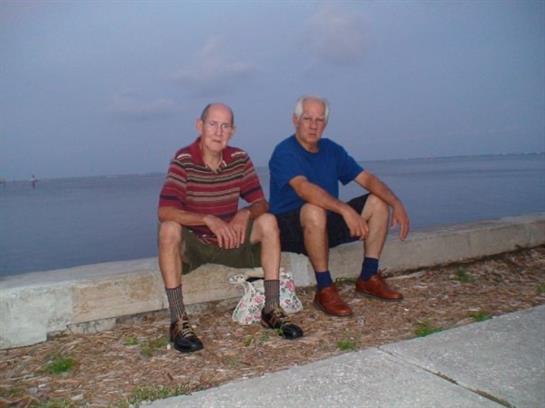 Two elderly men sit on a concrete ledge by the water, enjoying the quiet evening ambiance.