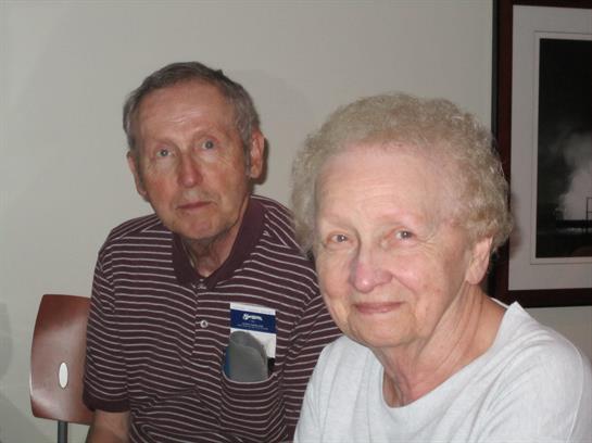 Two seniors share a warm smile while seated together in a comfortable space.